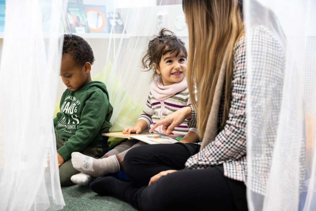 Pedagog läser bok tillsammans med två barn i läshörnan